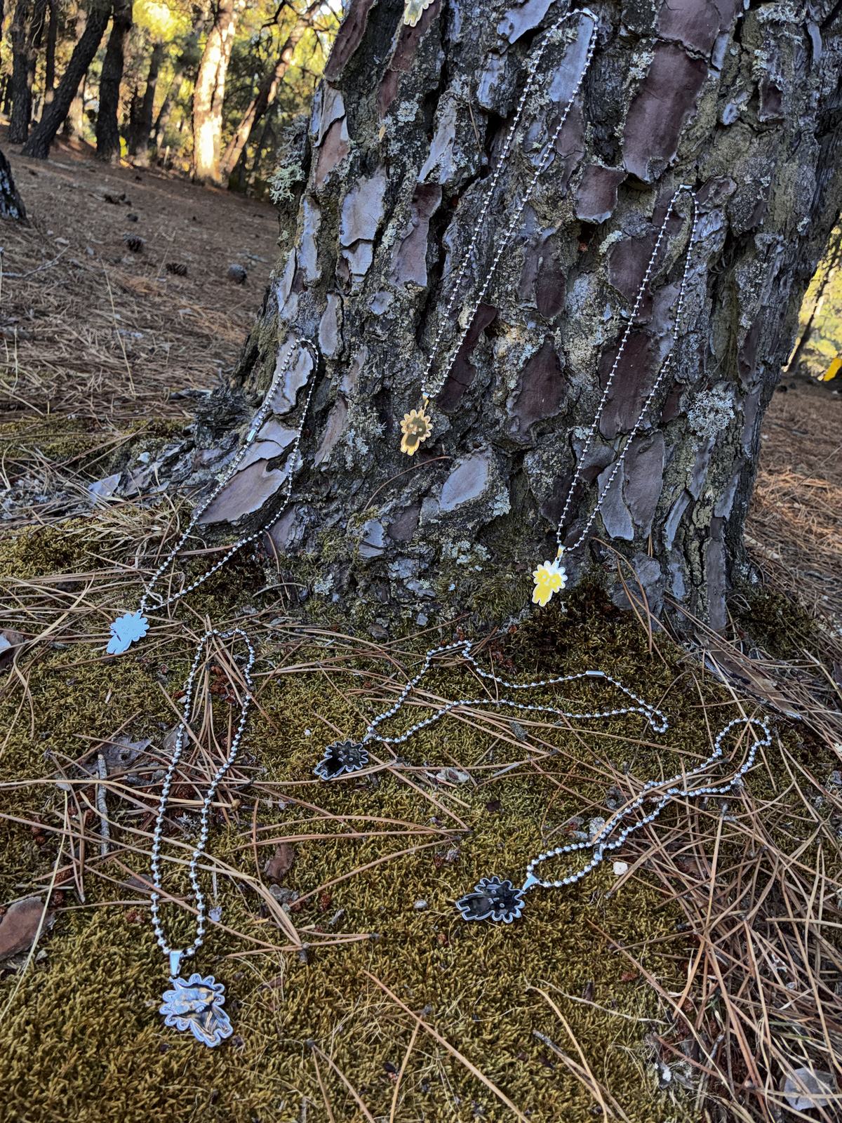 Varias cadenas MOSSCHAIN colgadas de un pino y sobre el musgo